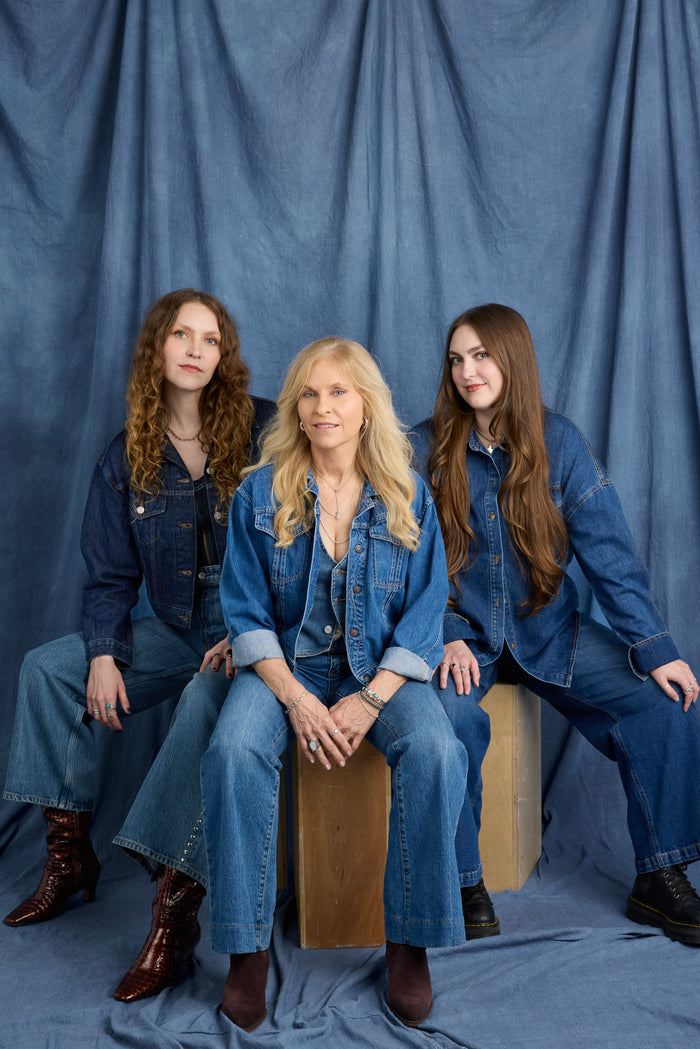 Founder Kris Kelly with her daughters in denim outfits sitting against a blue curtain.